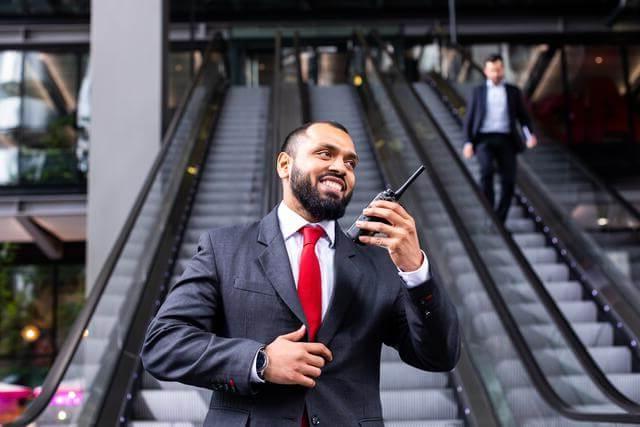 Security guard using a radio, standing at the bottom of escalators